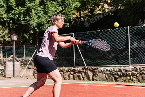 Preview: Female tennis player hitting ball with racket on clay court