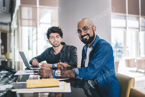 Preview: Smiling male coworkers using laptop in modern interior