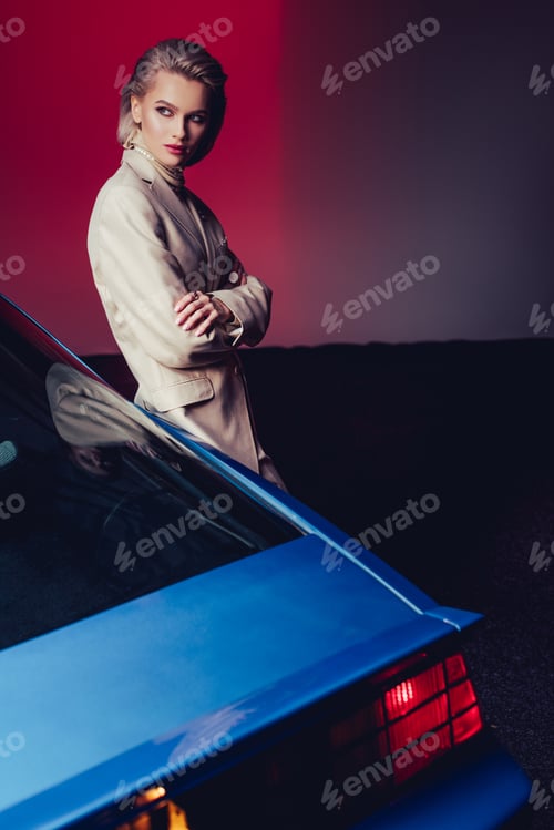 Preview: attractive and stylish woman with crossed arms in suit standing near retro car