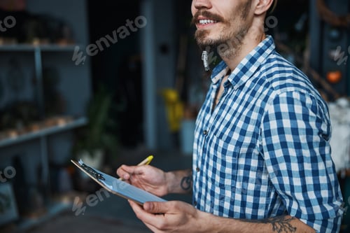 Preview: Joyful young man with clipboard standing in workshop