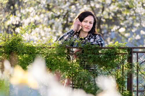 Preview: Young woman standing in spring park talking on her cellphone outdoors on warm day. Communication and