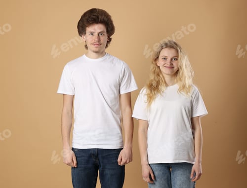Preview: Young woman and man wearing blank white t-shirts on light brown background. Mockup for design