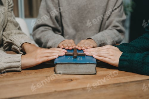 Preview: Group of Christians sit together and pray around a wooden table with blurred open Bible pages