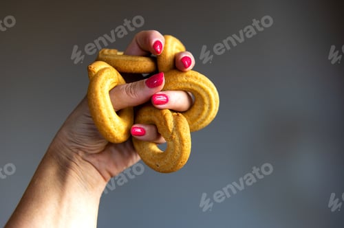 Preview: butter cookie rings on the fingers of a woman's hand on a gray background