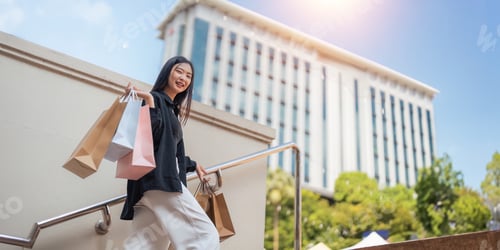 Preview: Happy beautiful young stylish woman with shopping bag while walking come out of mall on holiday