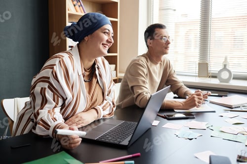 Preview: Smiling Muslim Woman Talking to Fellow Student Studying in Group Sitting at Table Indoors