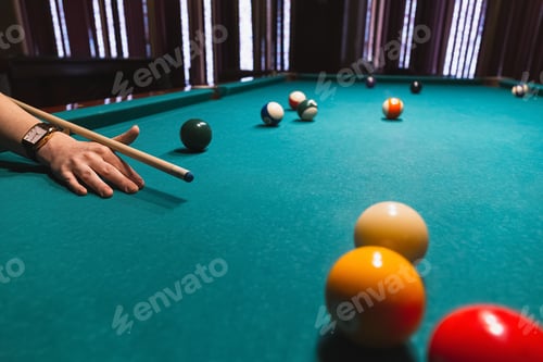 Preview: Player holding que and aiming to billiard white ball. White ball on green poll table.