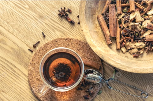 Preview: Cup of freshly brewed black tea, different types of spices on wooden table.