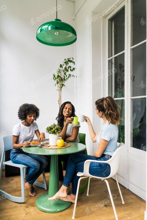 Preview: Three happy women sitting at table at home drinking coffee together