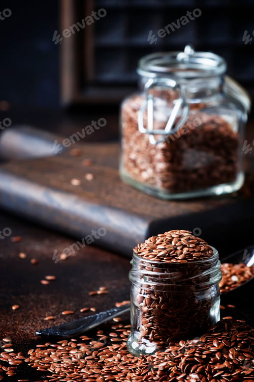 Preview: Flax seeds in glass jar, brown background, selective focus