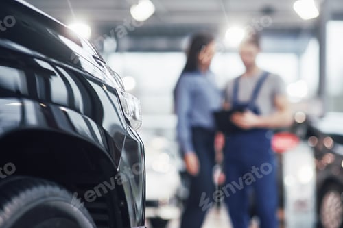 Preview: Beautiful young woman is talking to handsome car mechanic while repair a car in dealership