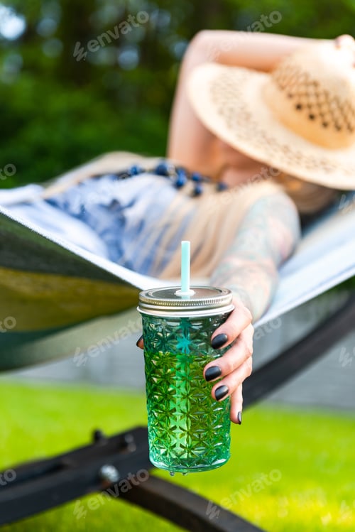 Preview: Tattooed Young Woman Relaxing on Hammock in Garden at Summer