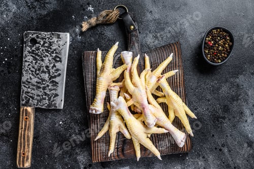Preview: Raw Chicken feets on butcher cutting board with cleaver. Black background. Top view
