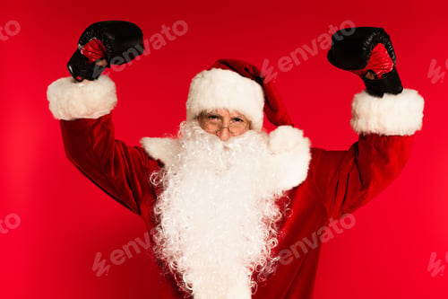 Preview: Santa claus in costume and boxing gloves showing muscles on red background