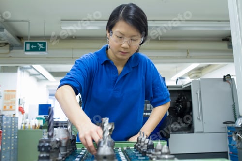 Preview: Young woman selecting metal components in industrial workshop