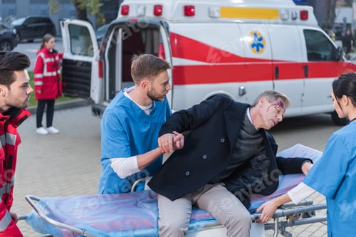 Preview: young paramedics helping injured man lie down on ambulance stretcher
