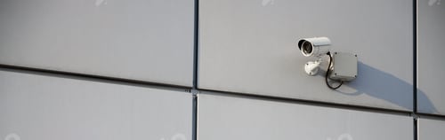 Preview: White surveillance camera built into the metal wall of the office building