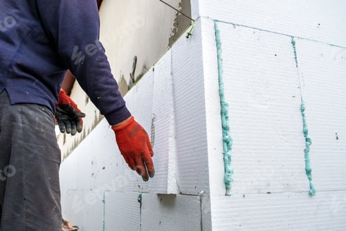 Preview: Construction worker installing styrofoam insulation sheets on house facade