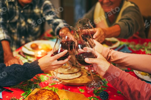 Preview: Happy family cheering with wine while eating Christmas holiday dinner together - Focus on right hand