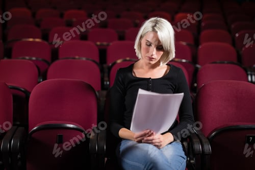 Preview: Woman wearing fitted black top reading script pages while sitting in red theater seats