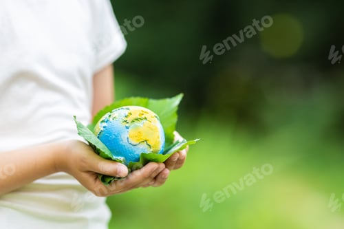 Preview: Kid holding small planet in hands against spring or summer green background. Ecology, environment