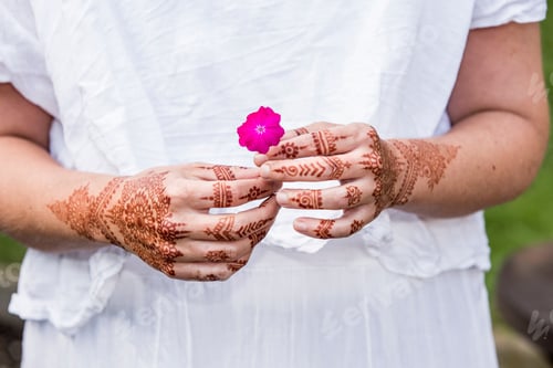 Preview: Woman in white dress with henna tattoo on hands holding flower