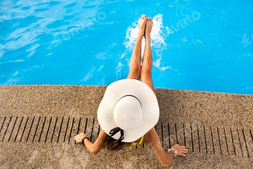Preview: Top down view of young woman wearing yellow straw hat resting near swimming pool with clear blue