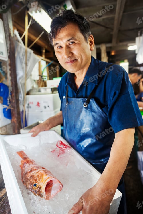 Preview: A traditional fresh fish market in Tokyo. a fish seller holding a bix of ice with a fresh fish.