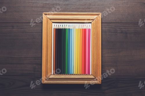 Preview: multicolored pencils in a frame over wooden background