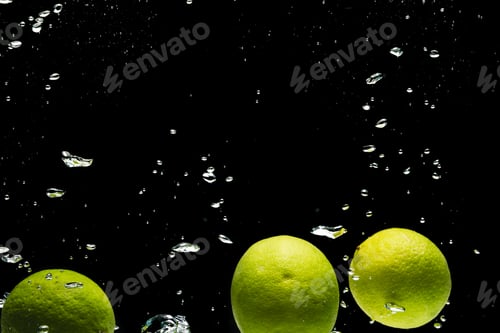 Preview: Close up of limes falling into water with copy space on black background
