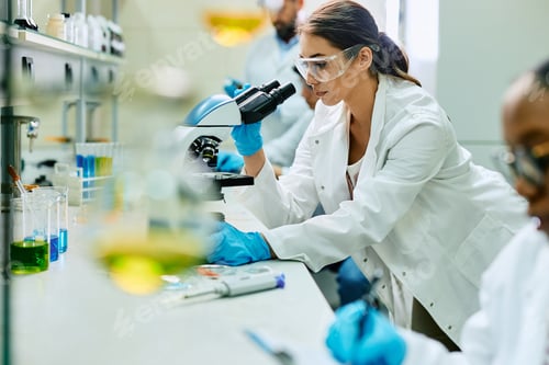 Preview: Young female biochemist using microscope during scientific research in laboratory.
