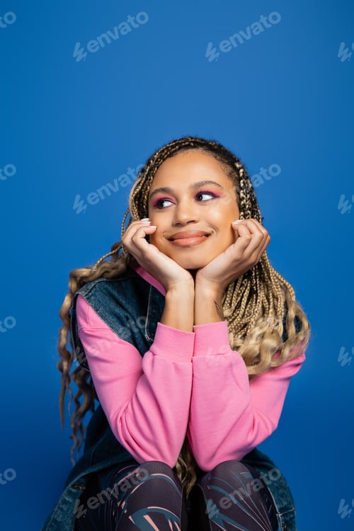 Preview: charming and dreamy african american woman with bold makeup looking away on blue background