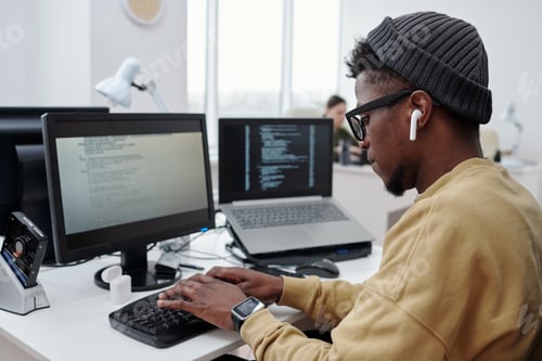 Preview: Side view of young man in casualwear listening to music in earphones at work