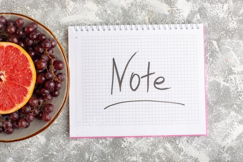 Preview: top view fresh grapefruit ring with red grapes and notepad on the white background citrus tropical