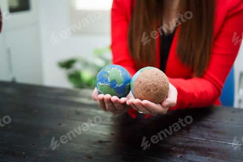 Preview: A young, smiling businesswoman holds a globe her desk, symbolizing global environmental awareness
