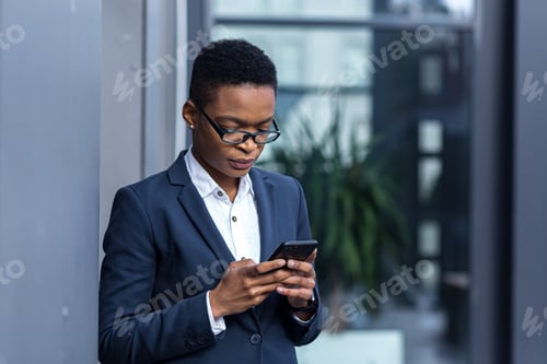 Preview: thinking business woman using phone, african american woman in business suit near office