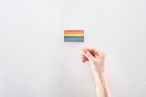 Preview: partial view of female hand with paper rainbow flag on grey background, lgbt concept