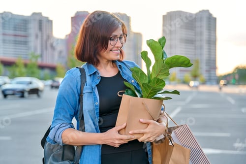 Preview: Middle aged woman with paper shopping bags with buying plant