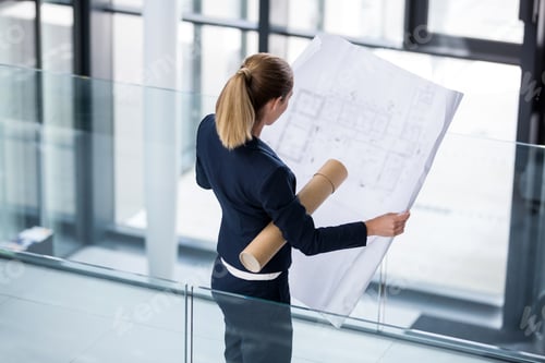 Preview: Businesswoman standing at office corridor with blueprint