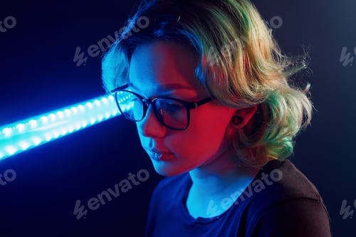 Preview: Portrait of young alternative girl in glasses with green hair in red and blue neon light in studio