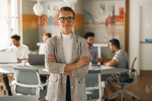 Preview: Portrait of smiling businesswoman in suit standing in modern office on colleagues background