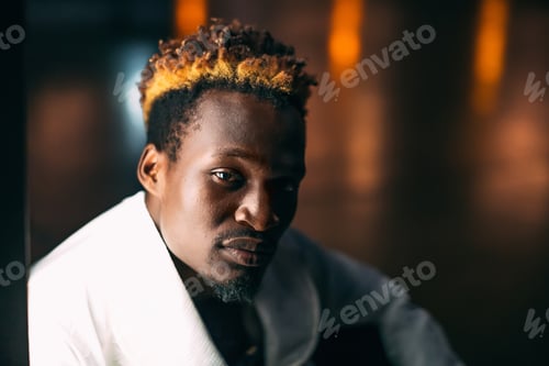 Preview: Portrait of young black man with colored hair sitting near lightbox at night