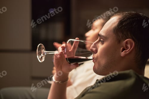 Preview: Young Caucasian Man Drinking Red Wine While Relaxing Indoors with Woman