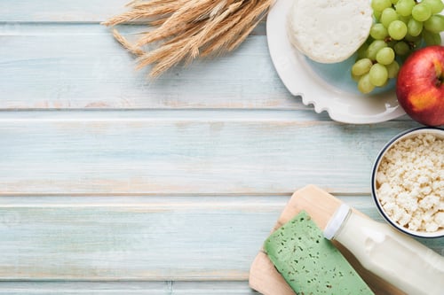 Preview: Shavuot jewish holiday celebration. Milk and cheese, ripe wheat and fruits, blue wooden background.
