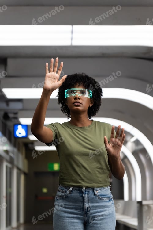 Preview: Serious afro woman wearing virtual reality simulators gesturing in futuristic metro station