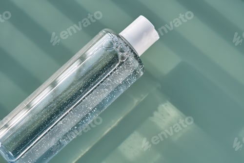 Vista previa: Bottle of facial toner or cleanser on a green background with stripes shadows.