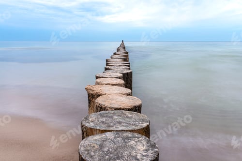 Preview: Wooden breakwater covered with moss, arranged in a row at sea, long exposure time, blurred sea waves