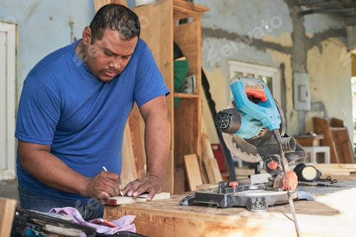 Preview: latin man marking the wood with the pencil, in the cabinetry workshop