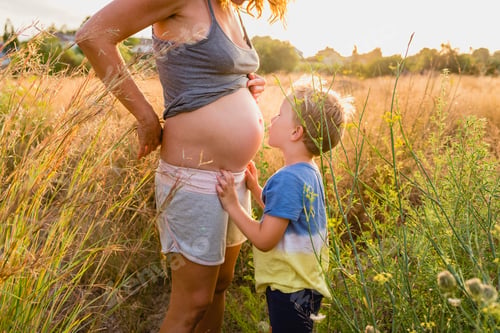 Preview: Child embraced his pregnant mother at sunset.