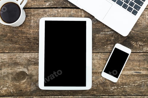 Preview: Desk setup featuring tablet, smartphone, laptop, and coffee cup on rustic wooden surface during